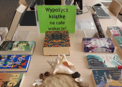 Na stole leżą rozłożone książki, które są częścią wystawy w Czytelni Neofilologicznej pt. Spakuj książkę na wakacje